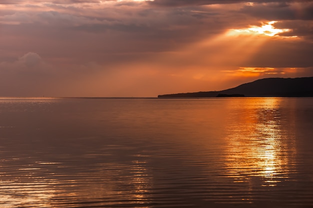 Lindo raio de sol saindo de trás das nuvens iluminando o oceano sereno