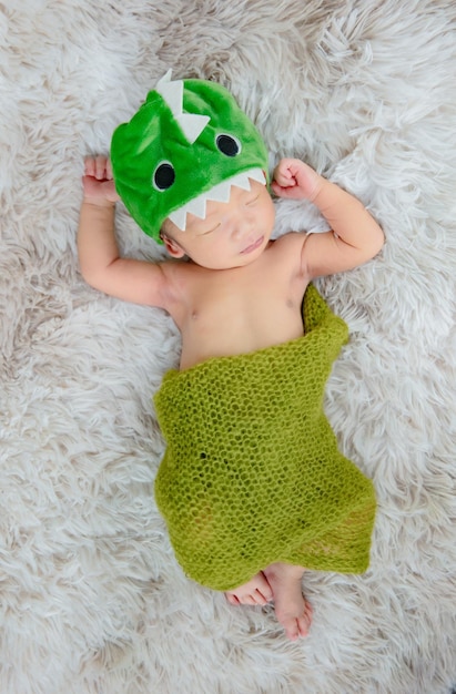 Lindo recién nacido con diadema de dinosaurio en alfombras de lana, concepto de moda