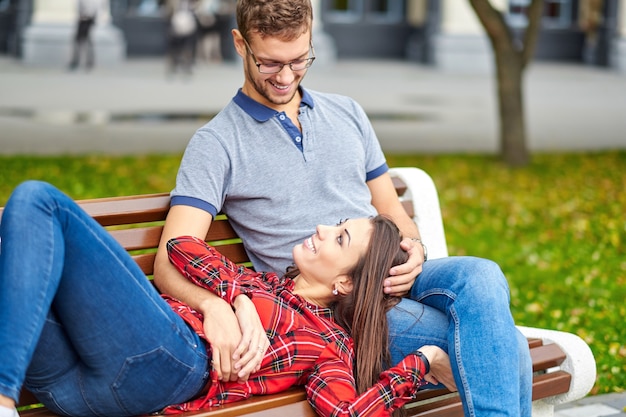 Lindo retrato de um jovem casal. Eles estão sentados no banco, se abraçando e se beijando.