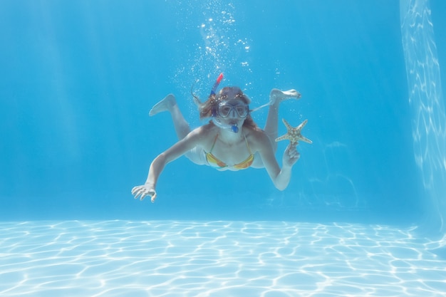 Lindo rubio subaquático na piscina com snorkel e estrela do mar