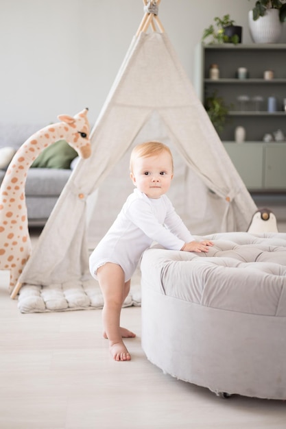 Un lindo y saludable bebé en una espaciosa y luminosa habitación para niños en casa con un wigwam, juguetes blandos, textiles para niños. El niño mismo está de pie con apoyo.