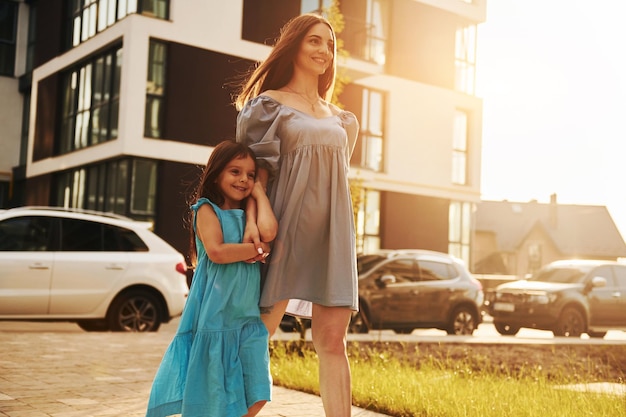 Lindo sol Jovem mãe com sua filha andando perto dos edifícios