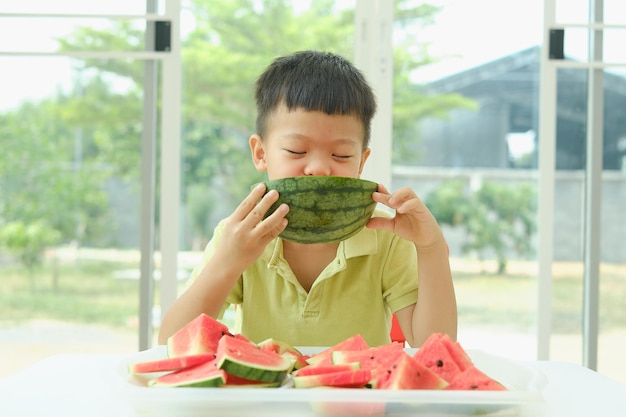 Lindo y sonriente niño de la escuela asiática comiendo sandía en verano