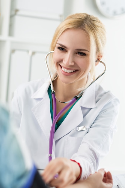 Lindo sorridente alegre médico em medicina feminina, medindo a pressão arterial para o paciente. Conceito médico e de saúde