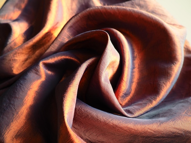 Lindo tecido - tafetá, suavemente dobrado em ondas. Material amassado que parece seda ou brocado. Estouro e gradiente de cor em diferentes ângulos de iluminação. Tecido para costurar roupas e cortinas.