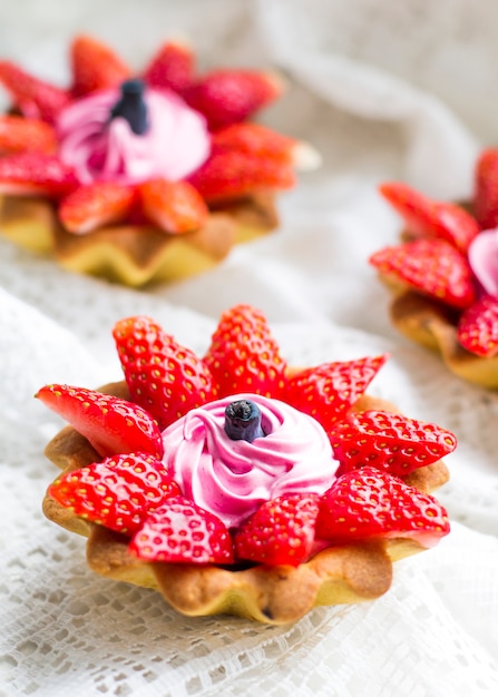 Lindos cupcakes saborosos perto com morangos, madressilva e creme-de-rosa