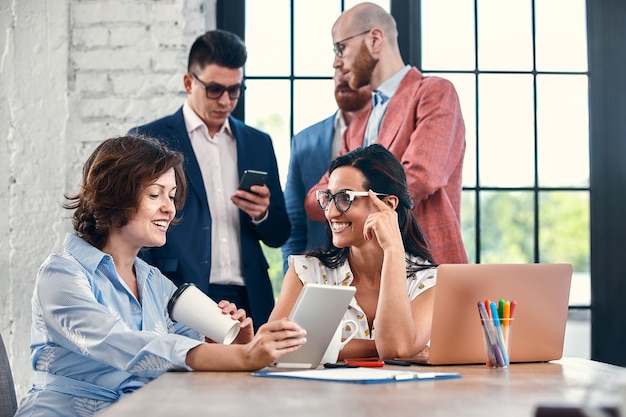 Lindos empresários estão usando gadgets, conversando e sorrindo durante a conferência no escritório