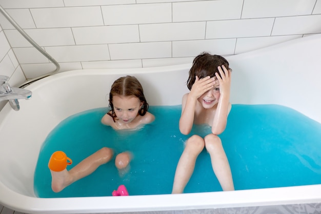 Lindos hermanos bañándose en la bañera juntos en agua azul