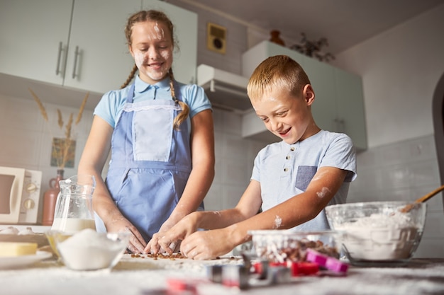 Lindos hermanos trabajando en hacer masa para galletas en la cocina