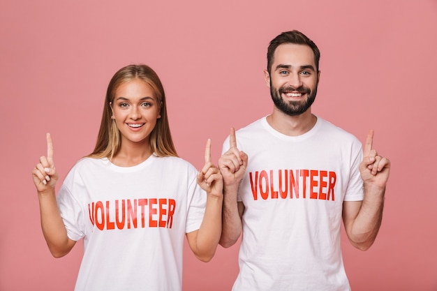 Foto lindos homens e mulheres voluntários vestindo camisetas de uniforme apontando os dedos para cima isolados