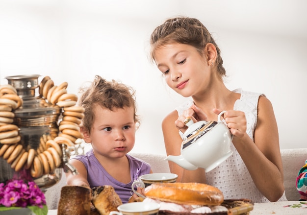 Lindos niños beben té sentados a la mesa