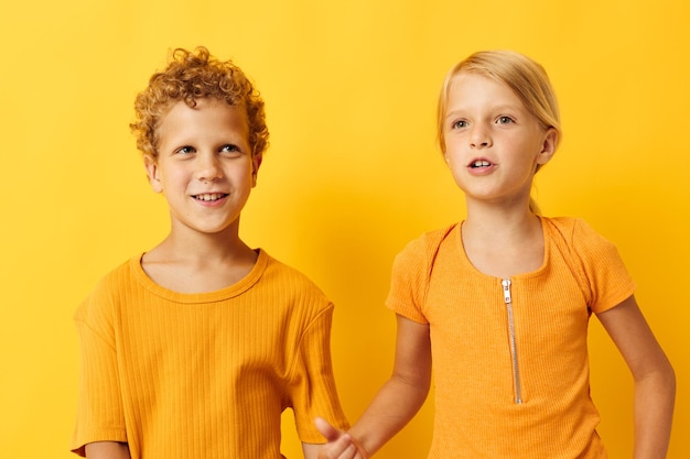 Lindos niños en edad preescolar en camisetas amarillas de pie lado a lado emociones infantiles fondo amarillo inalterado