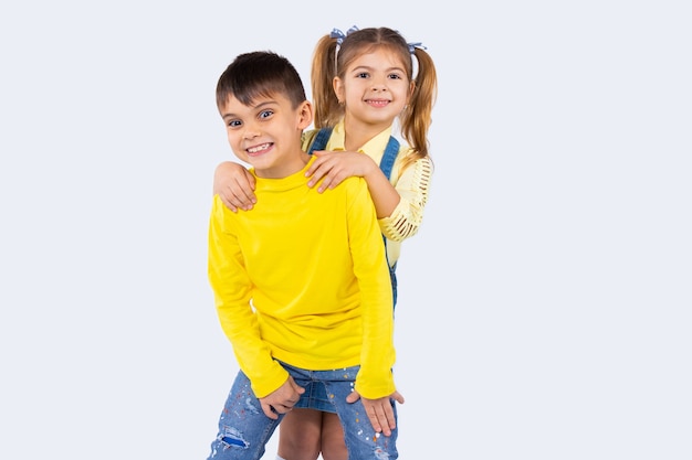 Foto lindos niños en edad preescolar sonriendo y posando en ropa casual sobre fondo blanco con espacio lateral.