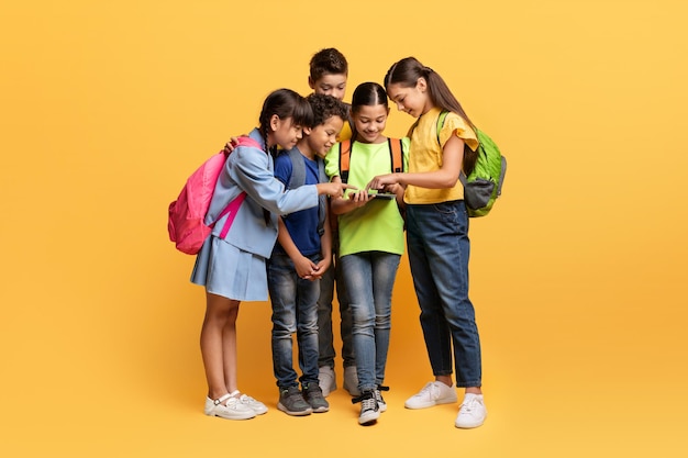 Lindos niños escolares multiétnicos mirando tableta digital en amarillo