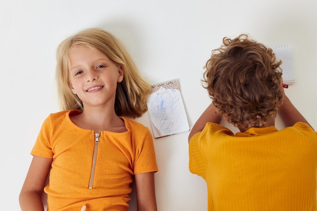 Lindos niños con estilo yacen en el suelo con blocs de notas y lápices estilo de vida infantil inalterado