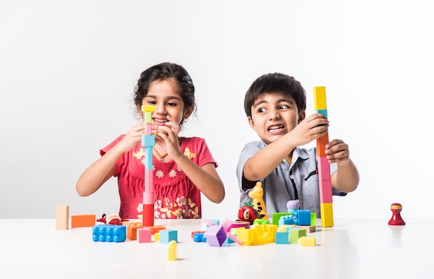 Lindos niños indios asiáticos jugando con coloridos juguetes o bloques de plástico mientras está sentado en la mesa o aislado sobre fondo blanco.