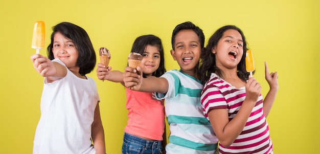 Lindos niños indios o asiáticos comiendo helado o barra de mango o dulces. Aislado sobre fondo de colores