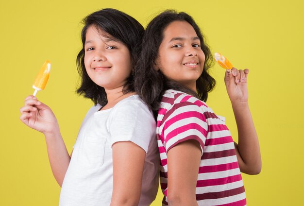 Lindos niños indios o asiáticos comiendo helado o barra de mango o dulces. Aislado sobre fondo de colores