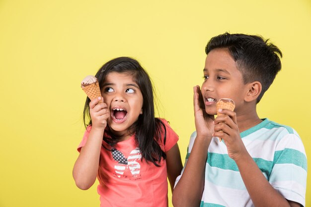 Lindos niños indios o asiáticos comiendo helado o barra de mango o dulces. Aislado sobre fondo de colores