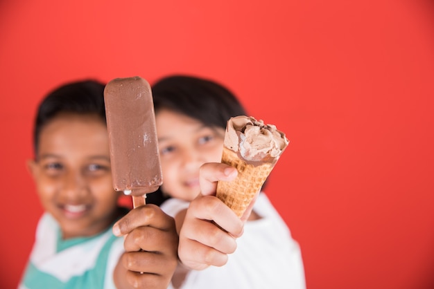 Lindos niños indios o asiáticos comiendo helado o barra de mango o dulces. Aislado sobre fondo de colores