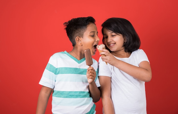 Lindos niños indios o asiáticos comiendo helado o barra de mango o dulces. Aislado sobre fondo de colores