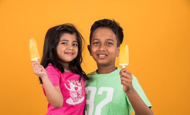 Lindos niños indios o asiáticos comiendo helado o barra de mango o dulces. Aislado sobre fondo de colores