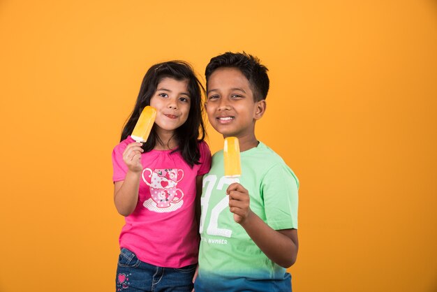 Lindos niños indios o asiáticos comiendo helado o barra de mango o dulces. Aislado sobre fondo de colores