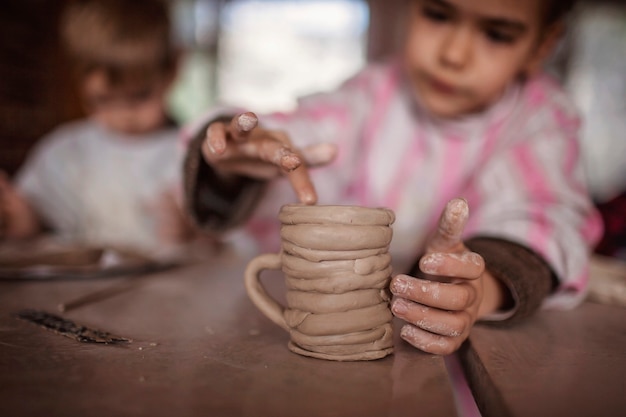 Lindos niños pequeños jugando junto con plastilina en el taller de cerámica, artesanía y arte de arcilla