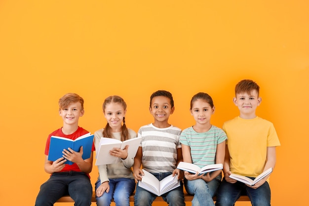 Lindos niños pequeños leyendo libros sobre la superficie de color
