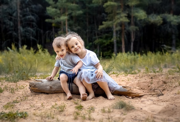 Lindos niños pequeños sentados en un tronco sobre un fondo de bosque