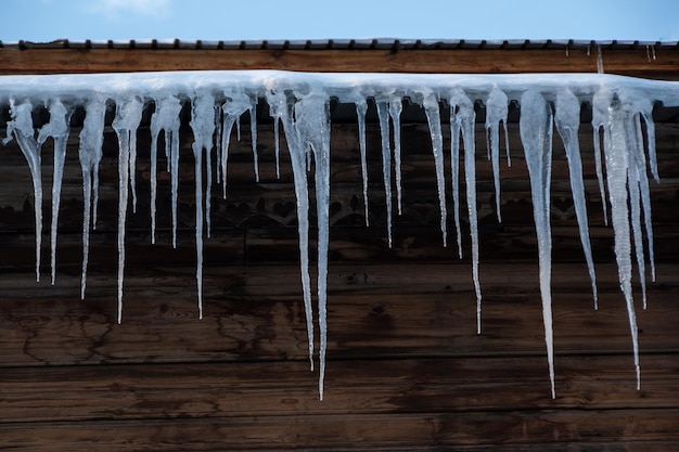 Lindos pingentes de gelo enormes pendurados no telhado do prédio Derretendo pingentes de gelo nos raios do sol da primavera