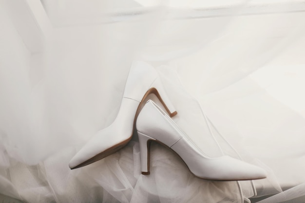 Lindos sapatos elegantes em vestido de noiva de seda de luxo planas sapatos brancos simples em vestido branco com ornamentos florais de renda vista superior dos preparativos nupciais da manhã