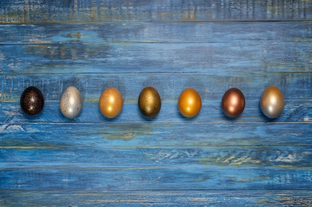 Línea colorida de huevos de pascua sobre fondo rústico de madera azul con espacio para copiar