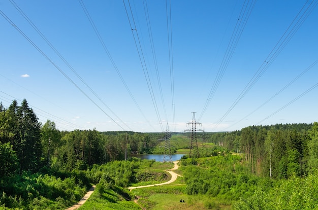 Foto línea eléctrica con el telón de fondo de un hermoso paisaje rural con un bosque y un pequeño lago en un día de verano.