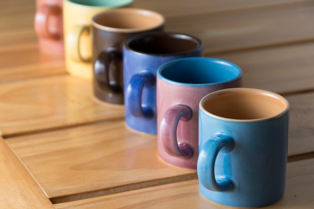 Línea formada por seis tazas de café de diferentes colores sobre una base de madera