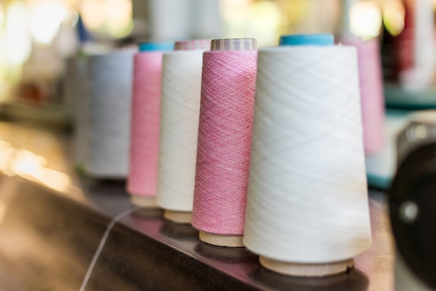 Línea de retroceso de carretes alternos de hilo de cachemira rosa y blanco en una fábrica de géneros de punto con enfoque selectivo en un carrete rosa