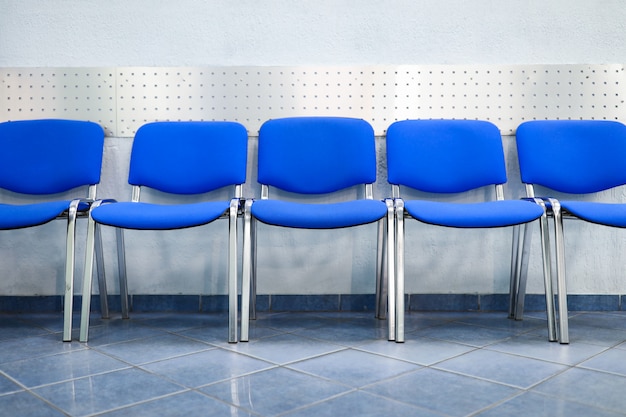 Foto línea de sillas de visitante azules vacías de pie cerca de la pared en la recepción o en primer plano del banco