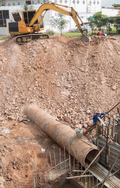 Foto línea de tubería de drenaje concreto debajo de la tierra cerca de la retroexcavadora en el área de la construcción.