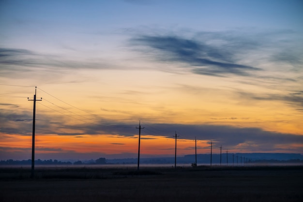 Líneas eléctricas en campo sobre fondo de amanecer