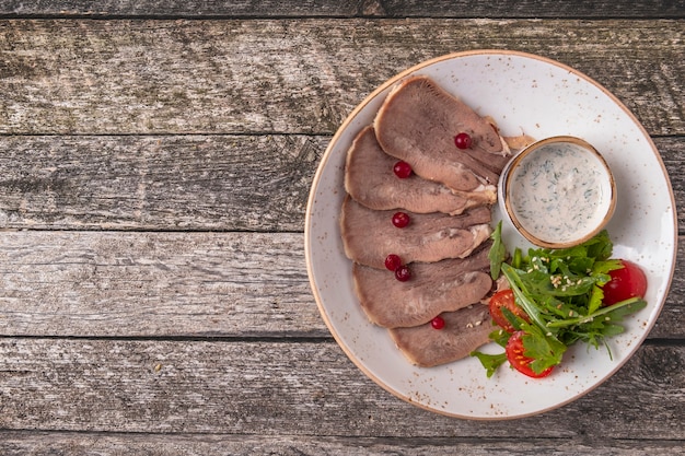 Língua de boi fatiada com cranberry, molho de raiz-forte e salada verde.