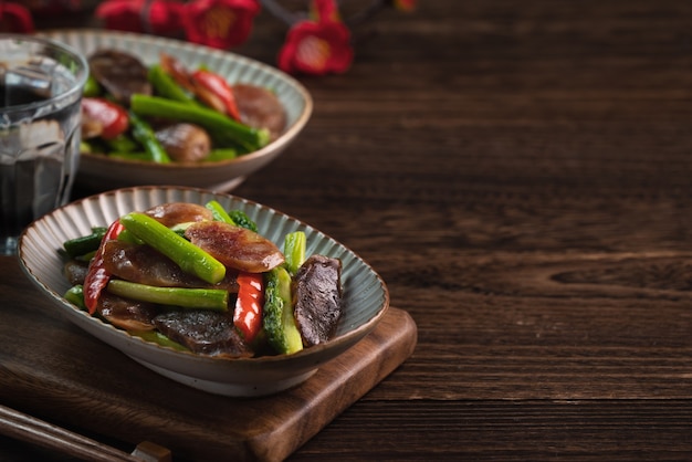 Linguiça chinesa defumada deliciosa e picante frita com espargos na mesa de madeira escura