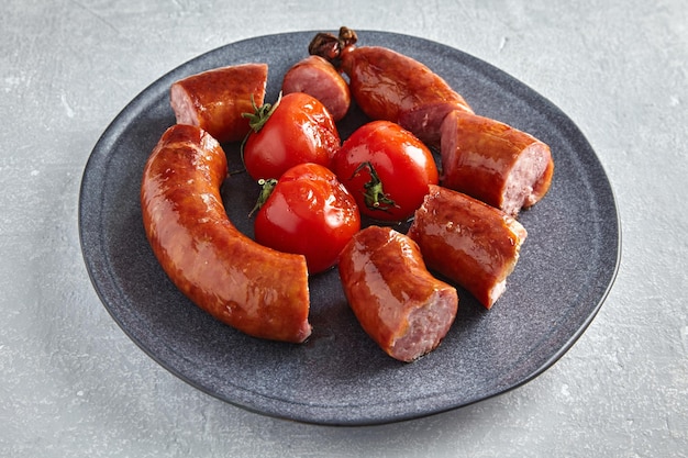 Linguiça de porco frita cortada em pedaços em um prato cinza com tomate