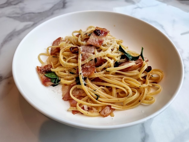 Linguine de pasta salteada con chile seco y tocino crujiente en un plato blanco