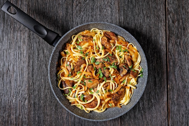 Linguini de pasta con hígado de pollo frito, cebolla caramelizada y perejil en una sartén, vista horizontal desde arriba, plano, espacio libre, cocina italiana