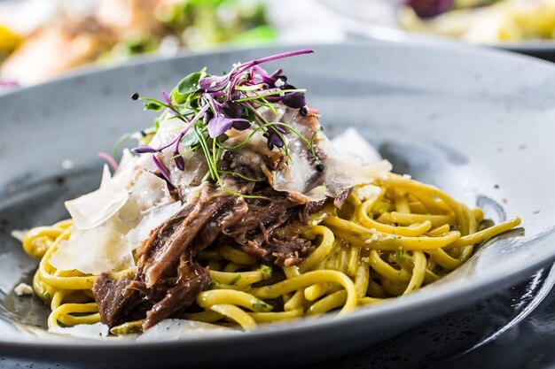 Linguini de pasta con pechuga de pato confitada, queso parmesano y decoración de hierbas.