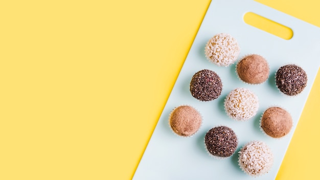 Foto linha de trufas de chocolate na tábua de cortar branca contra um fundo amarelo