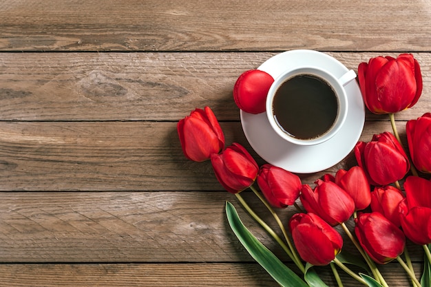 Linha de tulipas vermelhas e xícara de café preto americano em fundo de madeira