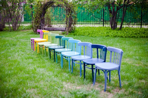 Linha diagonal de cadeiras de madeira coloridas no gramado no quintal, preparando-se para um micro cerimônia de casamento.