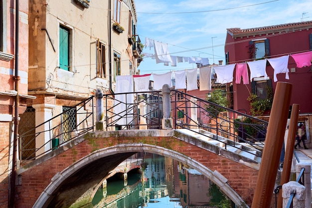 Linhas de lavagem através do canal em Veneza, Itália. Roupa pendurada em um varal entre os edifícios da cidade e acima da ponte. Varais entre janelas de antigas casas de tijolos em Veneza.