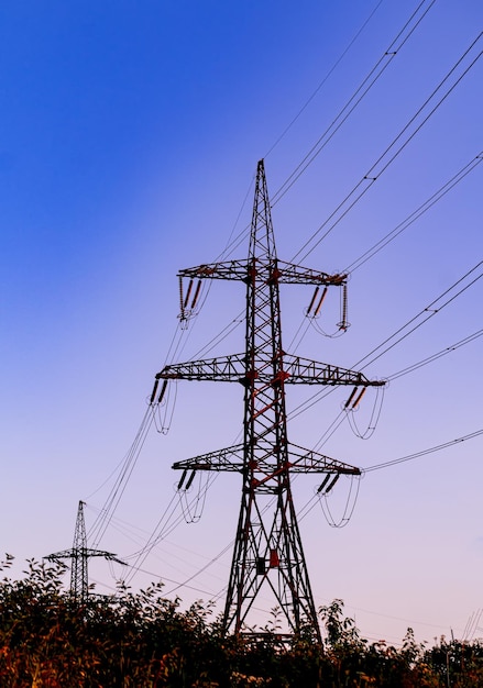 Linhas elétricas de alta tensão e tubos industriais com fumaça escura perto das torres elétricas de transmissão ao entardecer Poluição do conceito de atmosfera